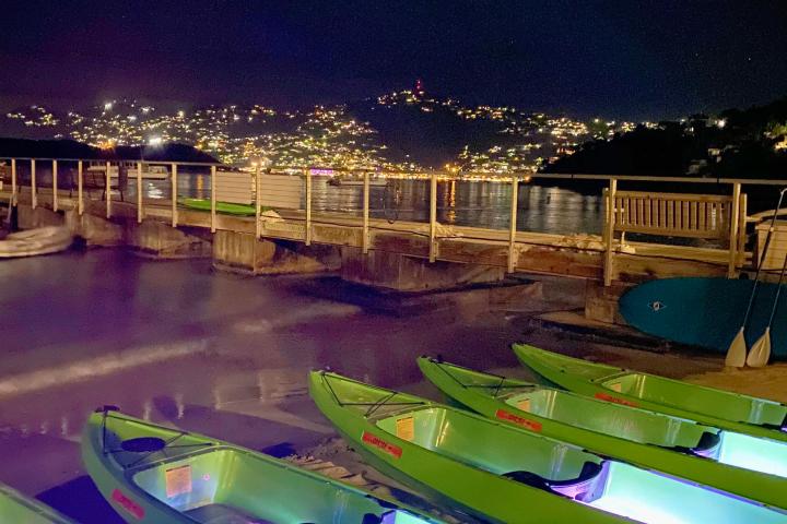 Illuminated kayaks on a dock at night with city lights in the background.
