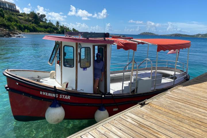 Red boat with white cabin docked beside a wooden pier on a sunny day.