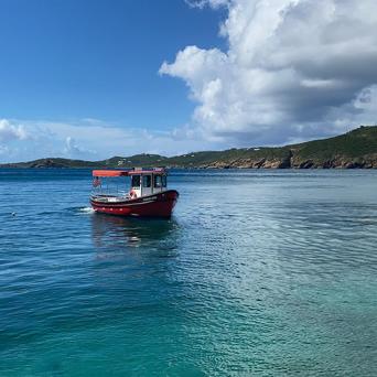 Red boat on clear blue sea with hilly coastline in background.