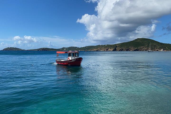 Red boat on clear blue sea with hilly coastline in background.