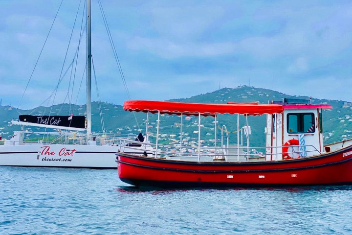Red boat and white catamaran on calm water with hills in background.