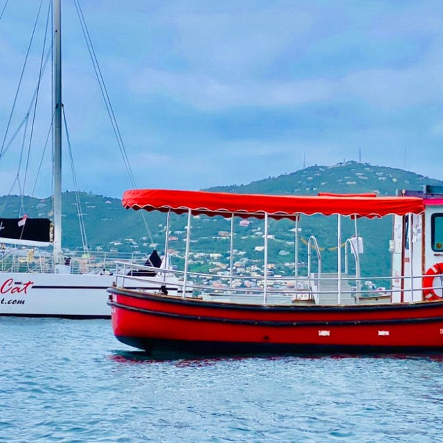 Red boat and white catamaran on calm water with hills in background.
