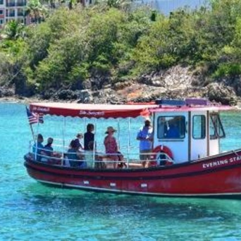 Red boat with passengers on clear blue water near a green hillside.