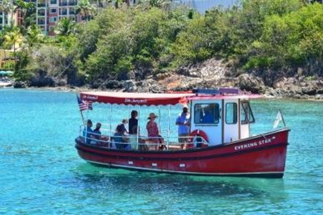 Red boat with passengers on clear blue water near a green hillside.