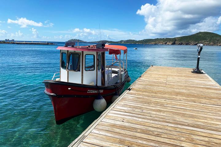 Red boat docked by wooden pier on a sunny day with mountains in background.