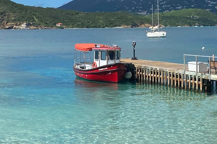 A red boat docked on a clear blue lake with a mountain backdrop.
