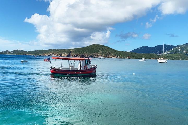 Small red boat on a clear blue sea under a partly cloudy sky.