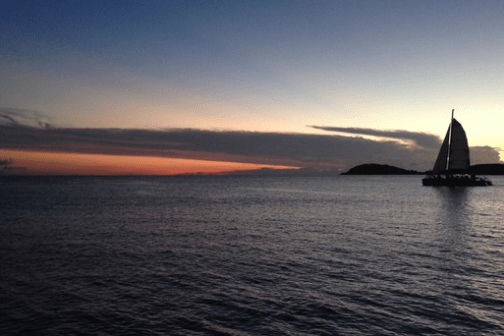Sailboat on calm sea at sunset with silhouette of distant hills.