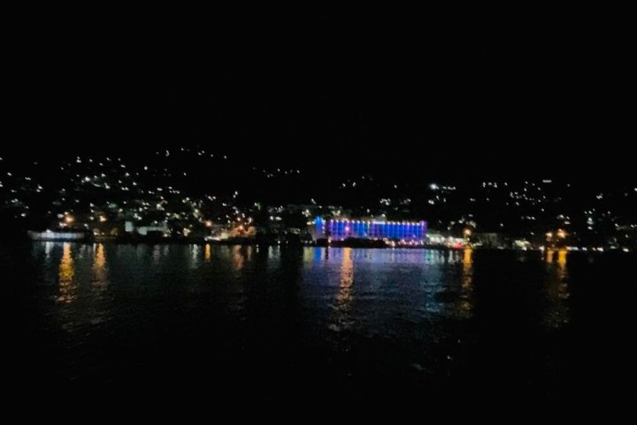 City waterfront at night with colorful lights reflecting on water.