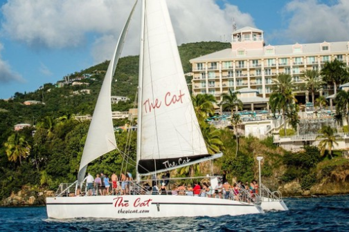 Sailboat near a tropical resort with lush greenery and a clear blue sky.
