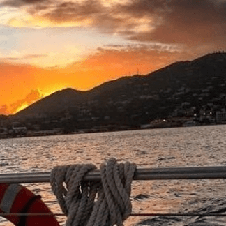 Sunset view from boat railing with mountains and water.