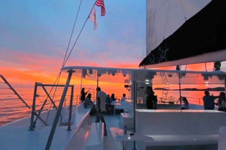 Sunset view from a sailboat deck with people and flags.