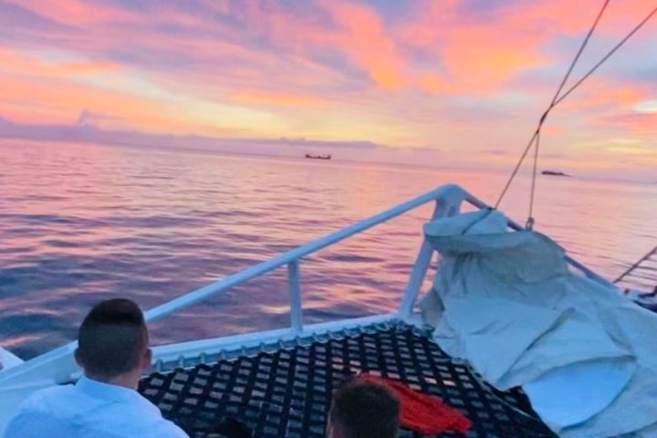 People relaxing on a boat at sunset with pink sky and calm sea.