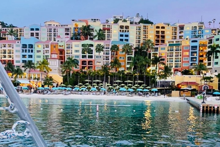 Colorful beachfront buildings with palm trees and beach umbrellas at sunset.