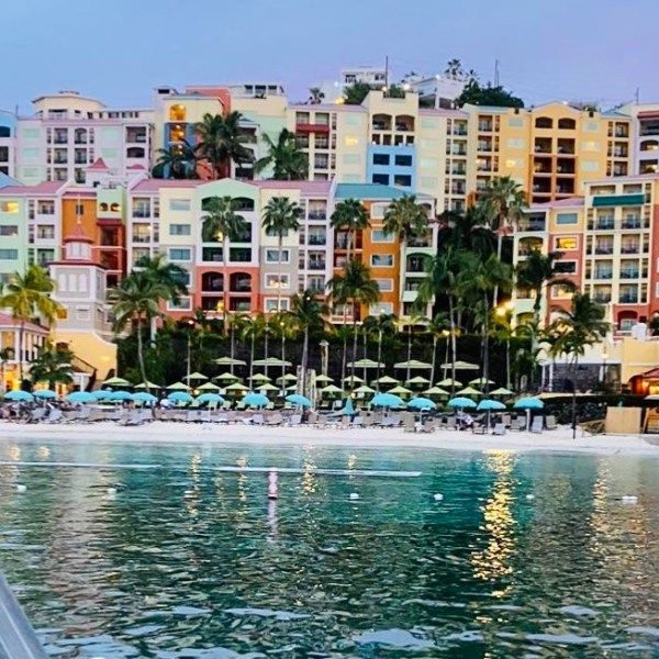 Colorful beachfront buildings with palm trees and beach umbrellas at sunset.