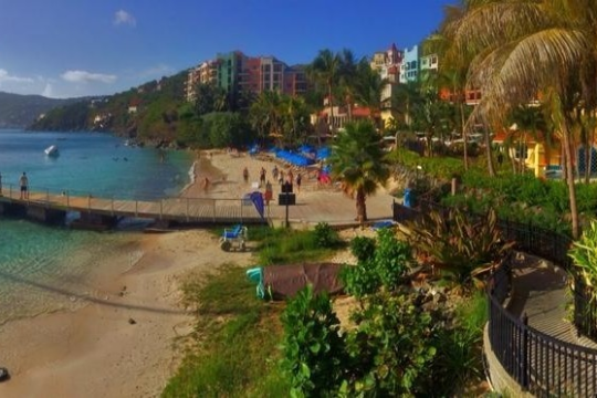 Tropical beach with clear water, umbrellas, palm trees, and colorful buildings.