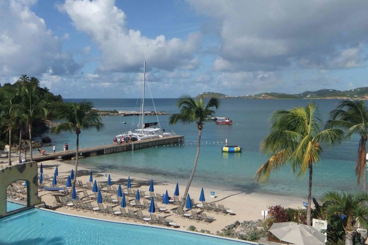 Tropical beach scene with palm trees, lounge chairs, and boats on the water.