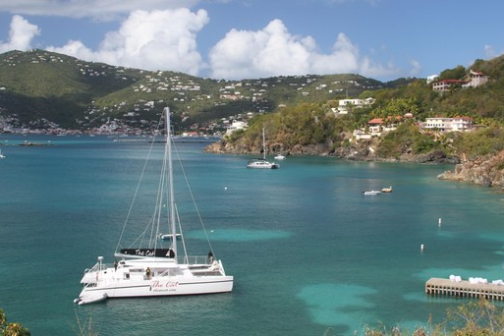 Sailboats anchored in a clear turquoise bay with hills in the background.