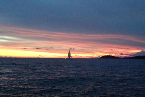 Sailboat on ocean at sunset with vibrant sky colors.