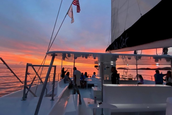 People on a boat enjoying a sunset under a colorful sky with an American flag flying.
