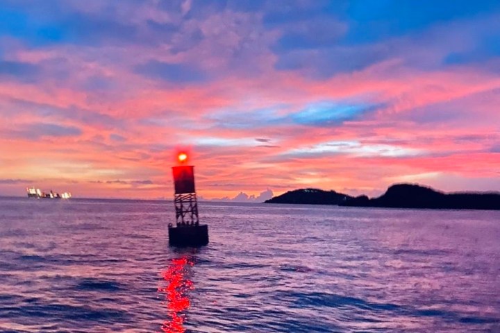 Sunset over the ocean with a red buoy, vibrant sky, and island silhouette.