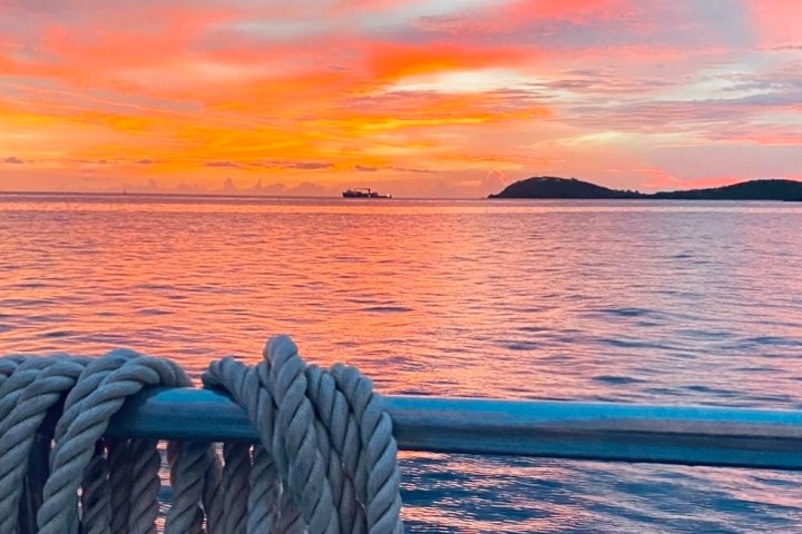 Sunset over ocean with dock rope in foreground and distant islands.