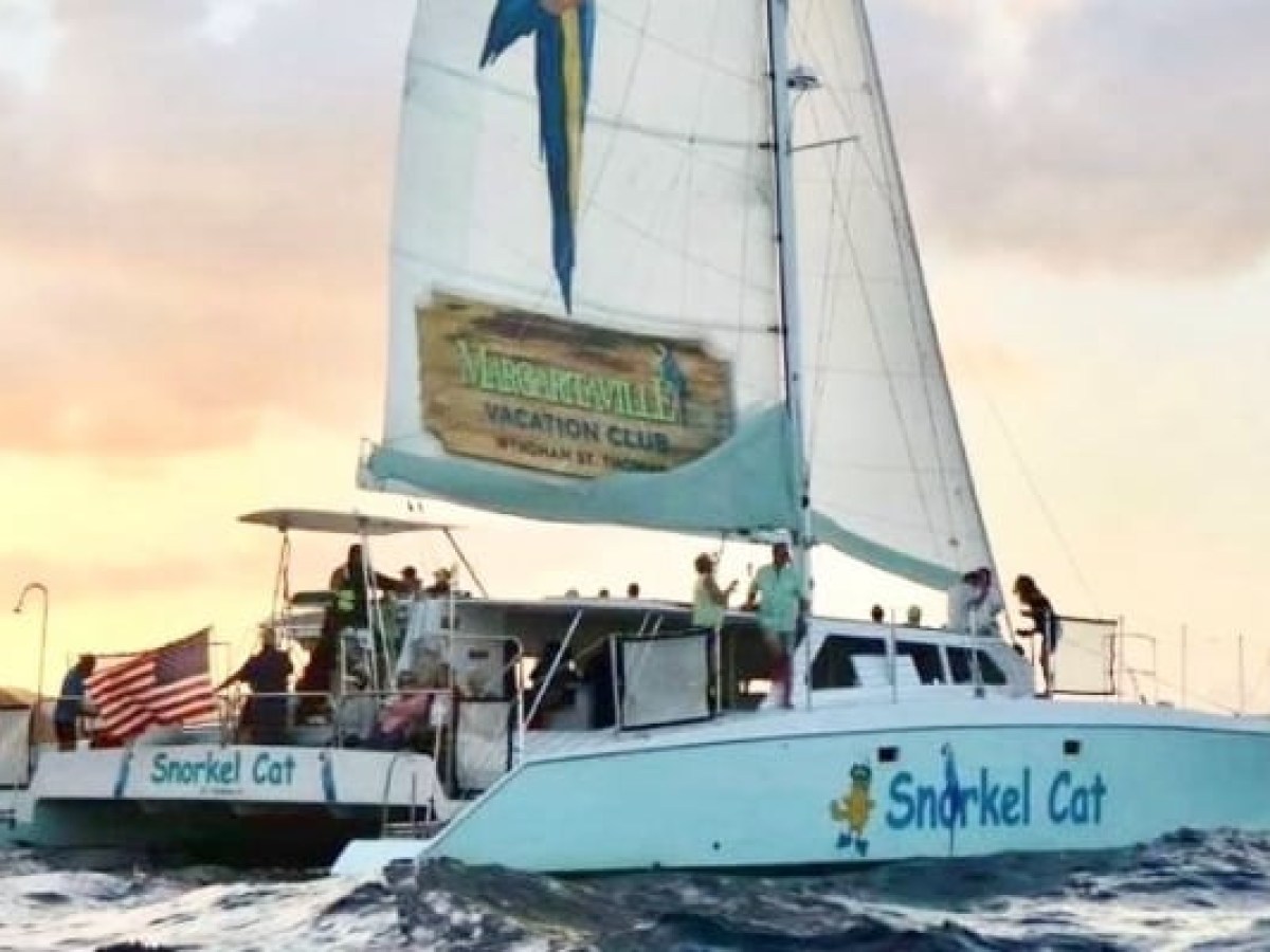 A catamaran sailing on water with 'Snorkel Cat' signage and people on board at sunset.
