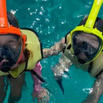 Two people snorkeling in clear blue water, wearing vests and snorkels.