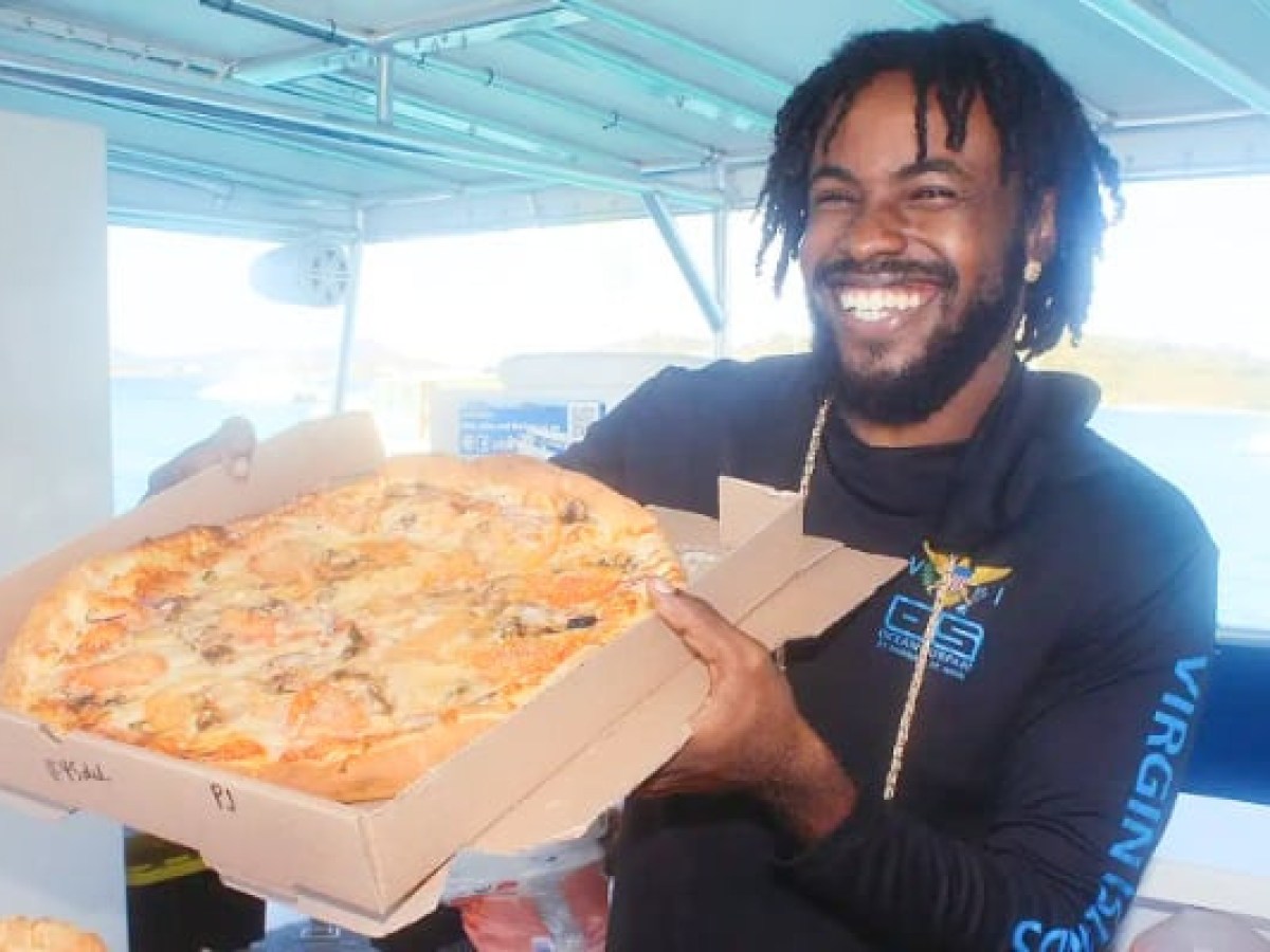 Person smiling and holding a large pizza box on a boat.