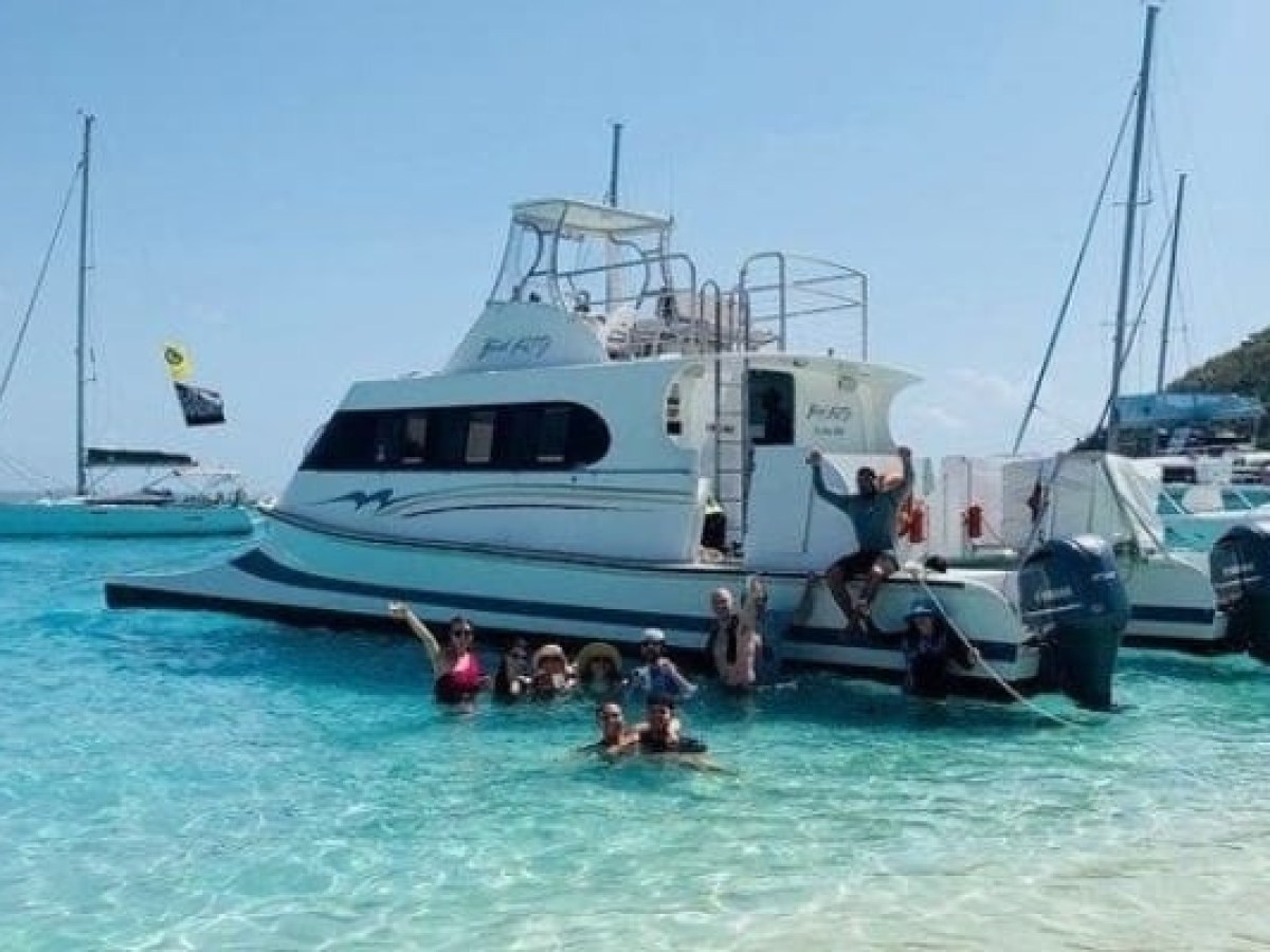Group swimming near a white boat in clear blue water.
