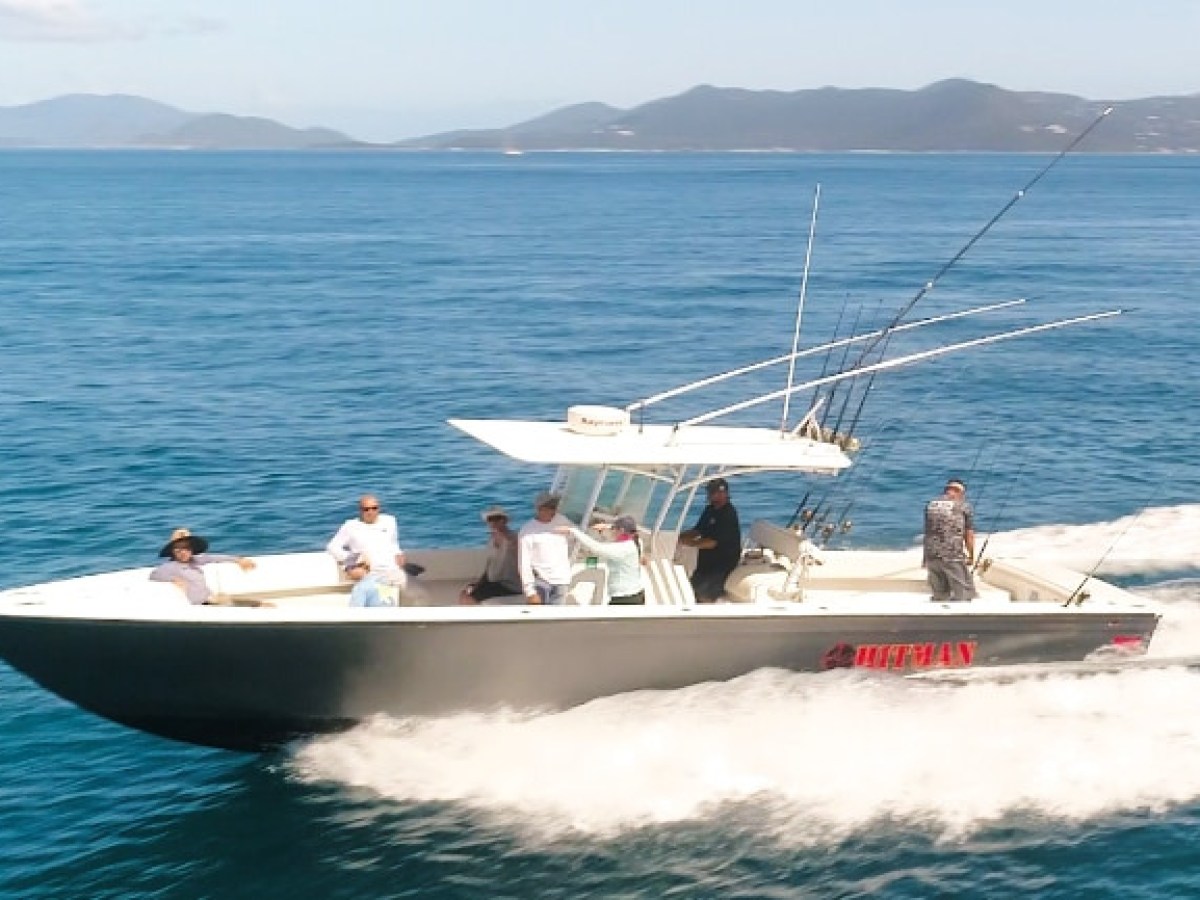 Boat with six people fishing on blue ocean, hills in background.
