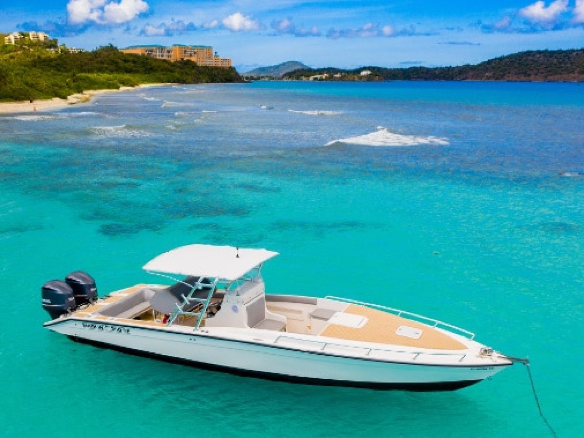 Boat anchored in turquoise water near a sandy beach and green hills.