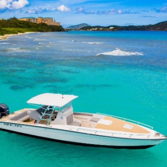 Boat anchored in turquoise water near a sandy beach and green hills.