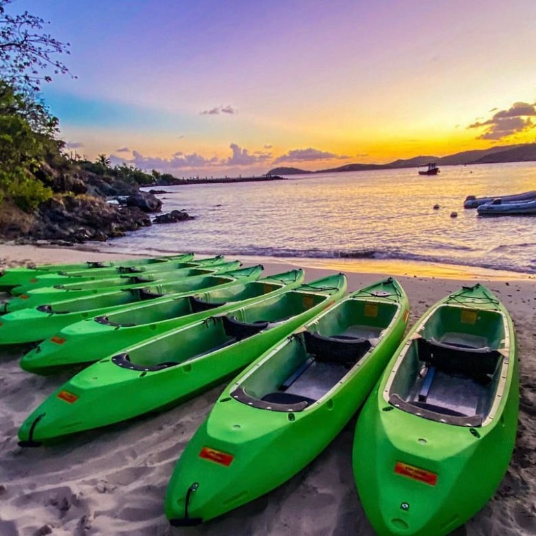 Nine green kayaks on a sandy beach at sunset, calm water in background.