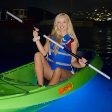 Person kayaking on illuminated water at night with city lights in background.
