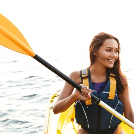 Smiling woman kayaking on water with yellow paddle.