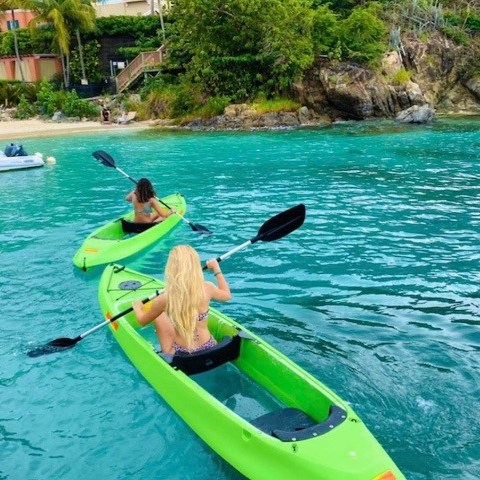 Two people kayaking on clear turquoise water near a tropical shoreline.