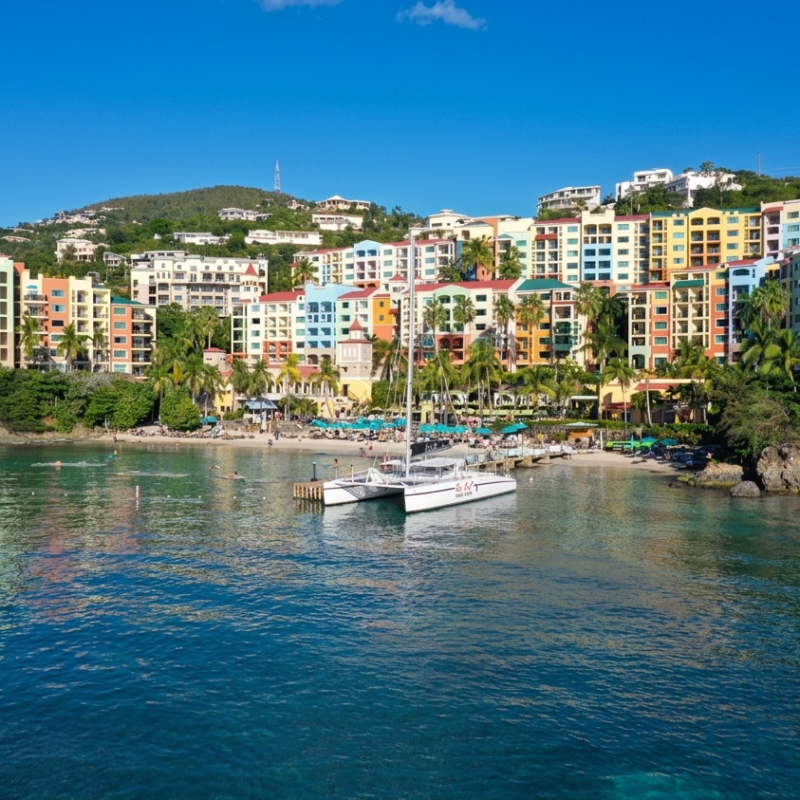 Colorful buildings overlook a bay with a catamaran in clear blue water.