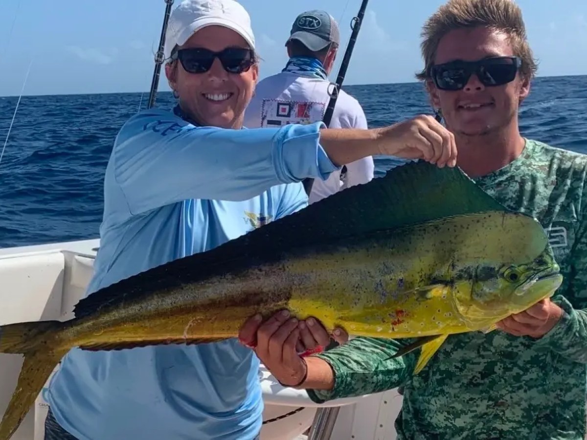 Two people on a boat proudly holding a dolphinfish.