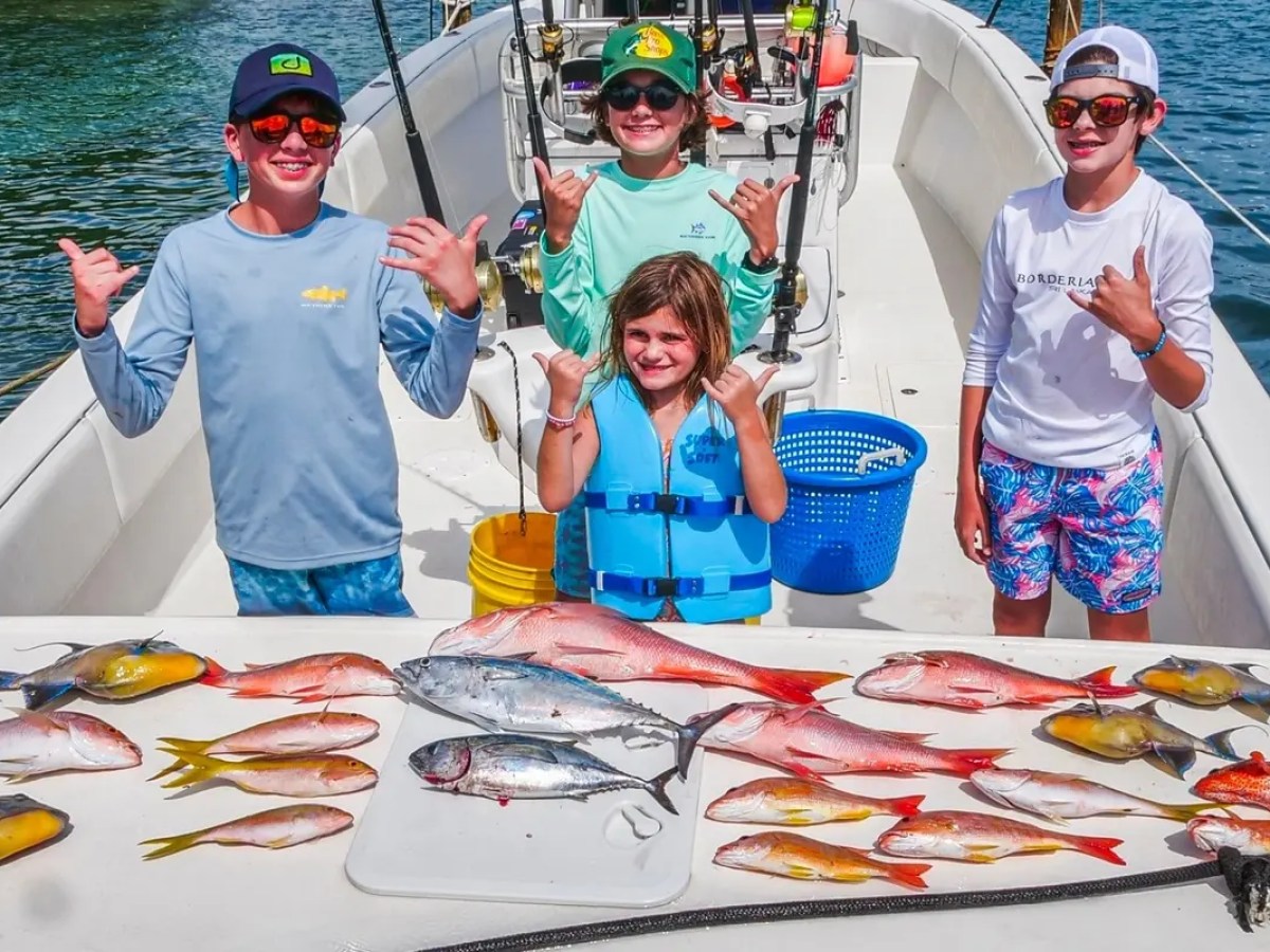 Four kids on a boat displaying a colorful fish catch.