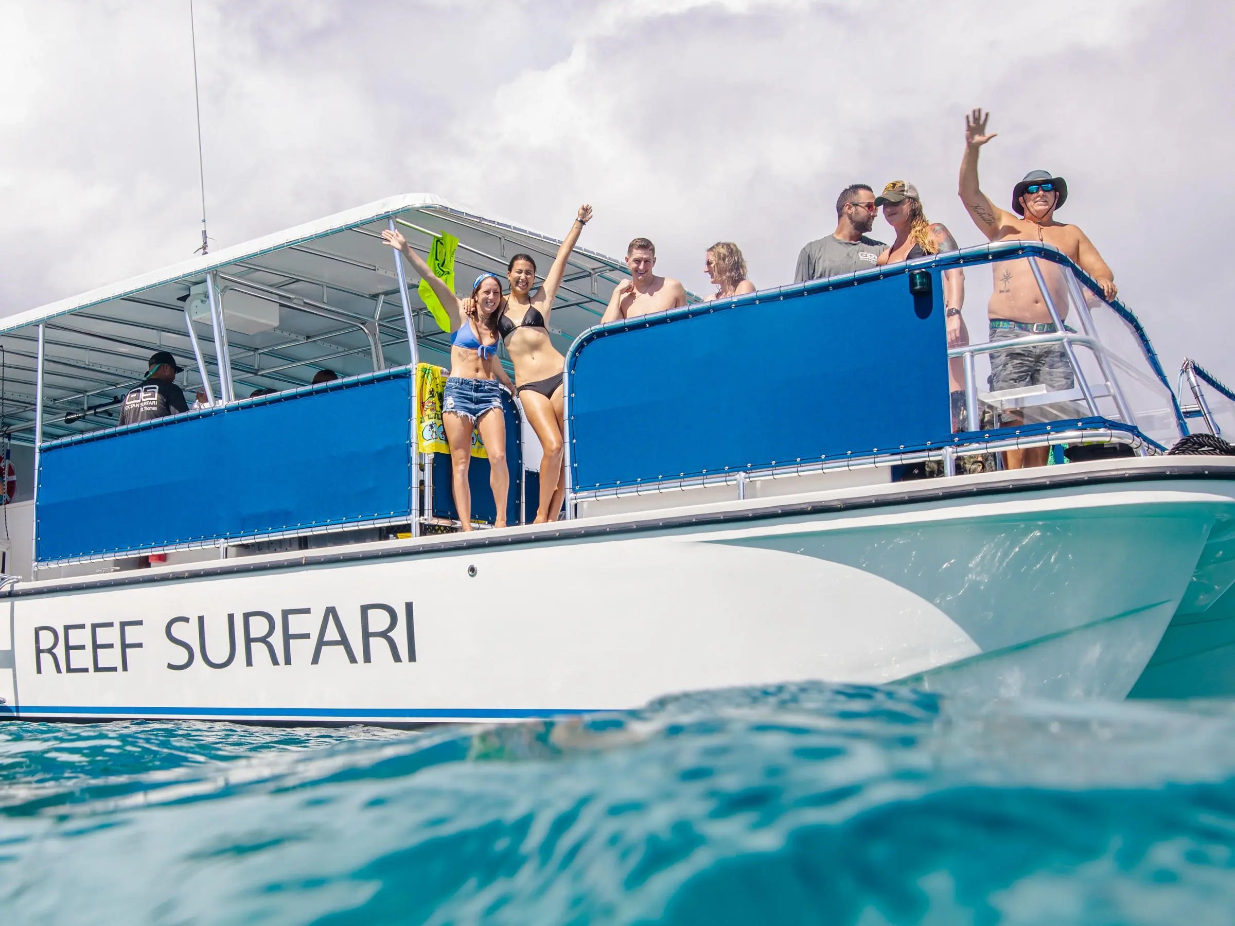 People waving on a boat named Reef Surfari in the ocean.