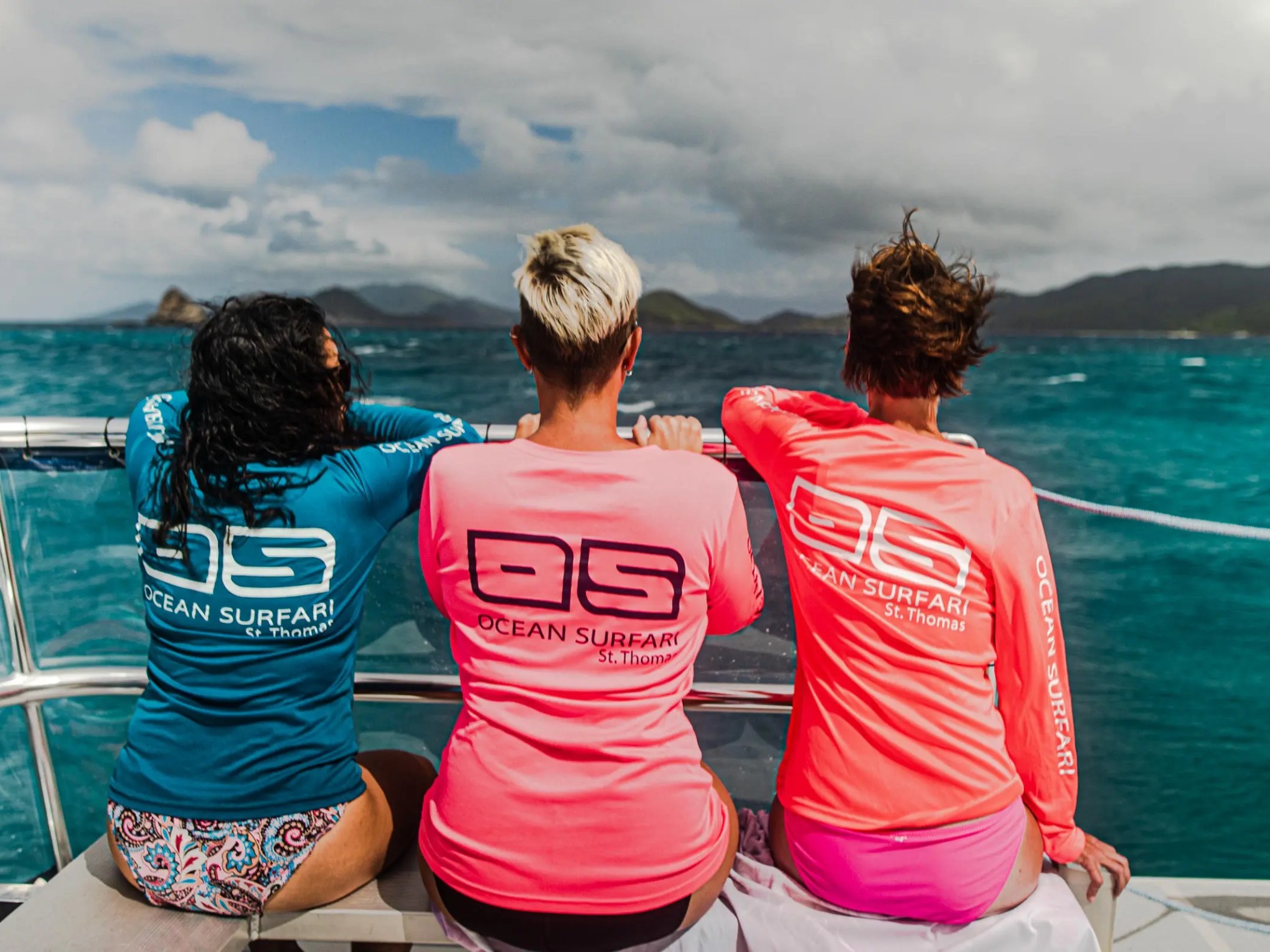 Three people on a boat wearing Ocean Surfari shirts, looking at the ocean.