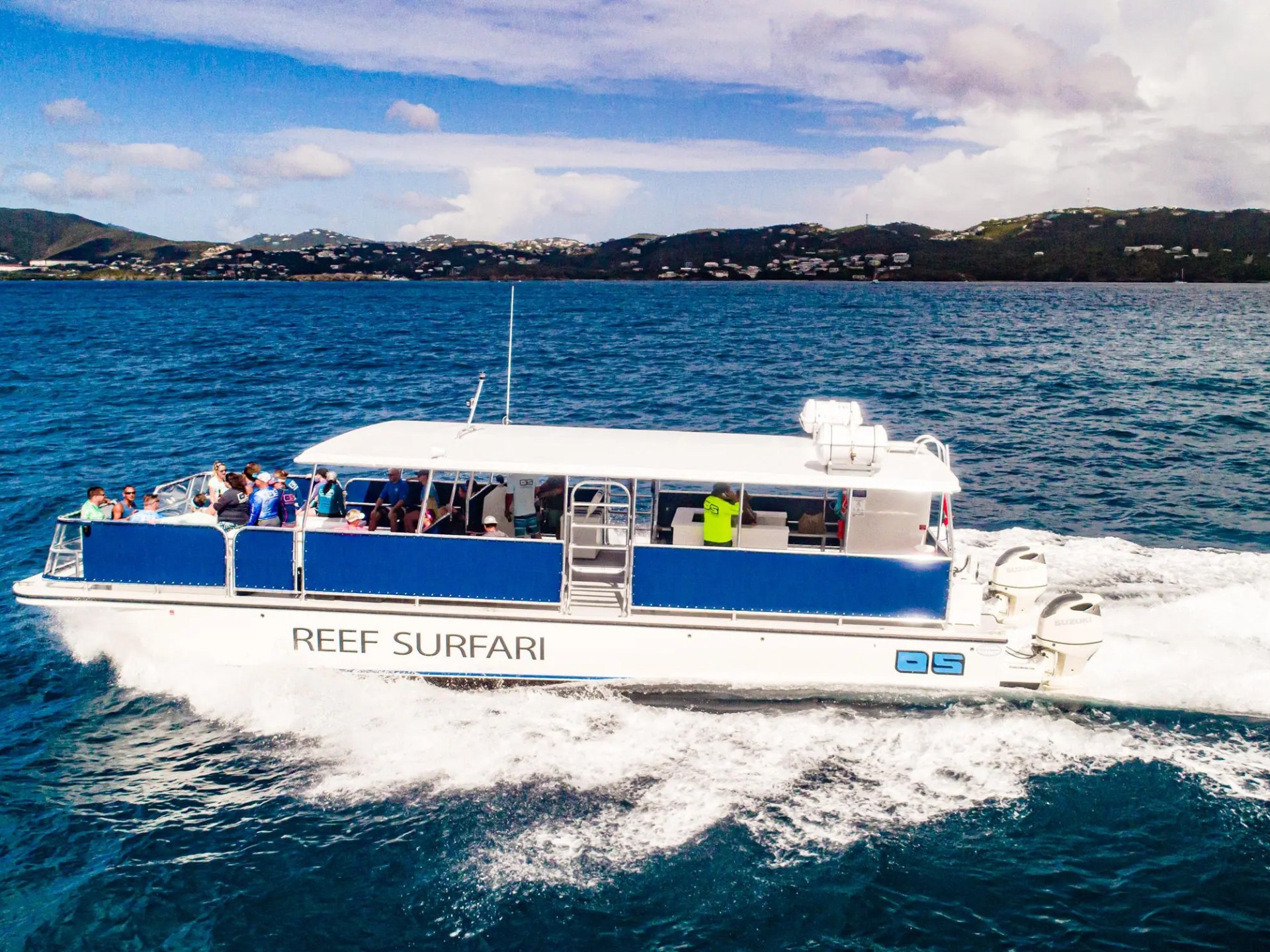 White boat named Reef Surfari cruising on blue ocean with hills in background.