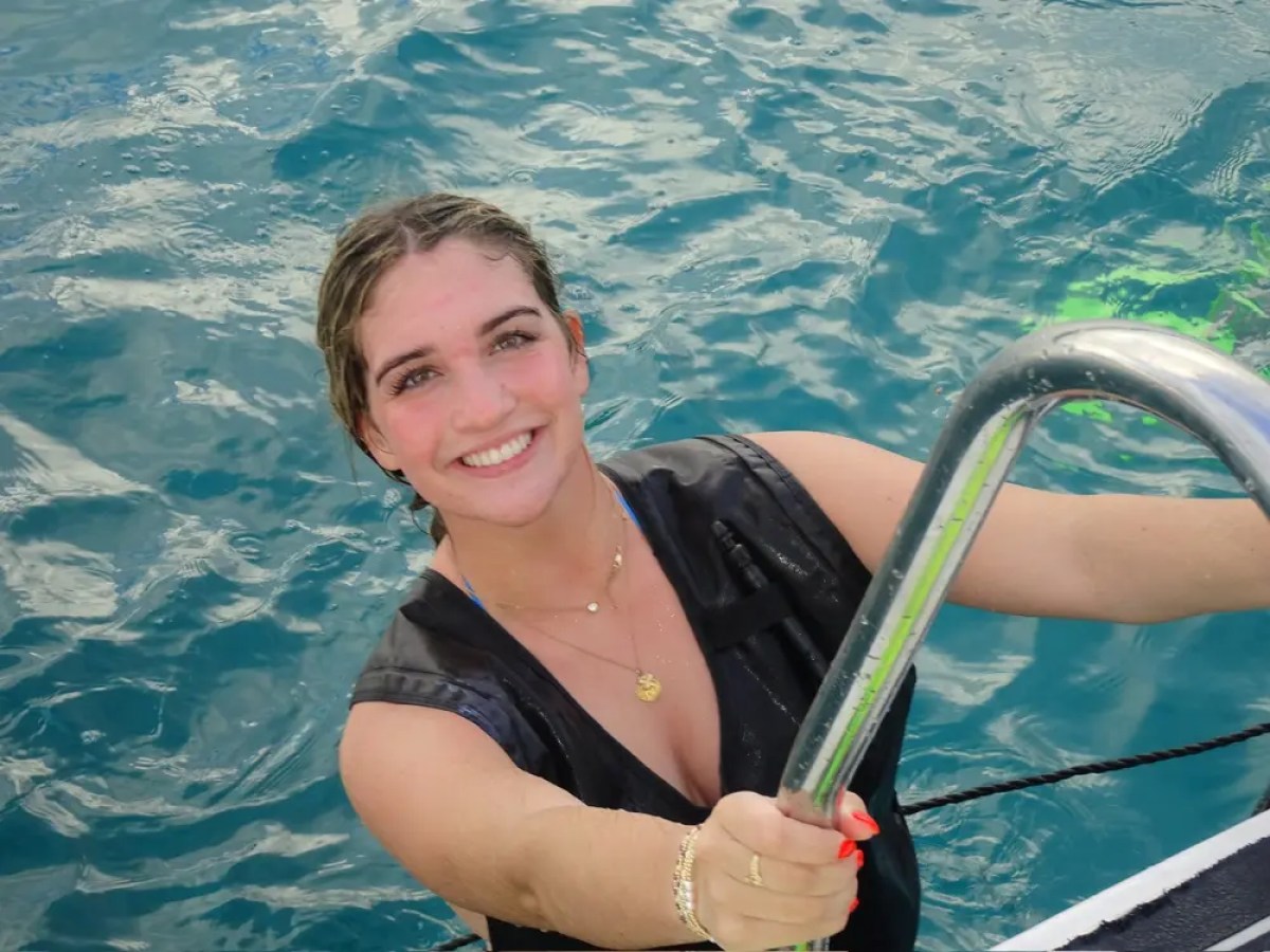 Person smiling in water, holding a ladder, wearing a life vest.