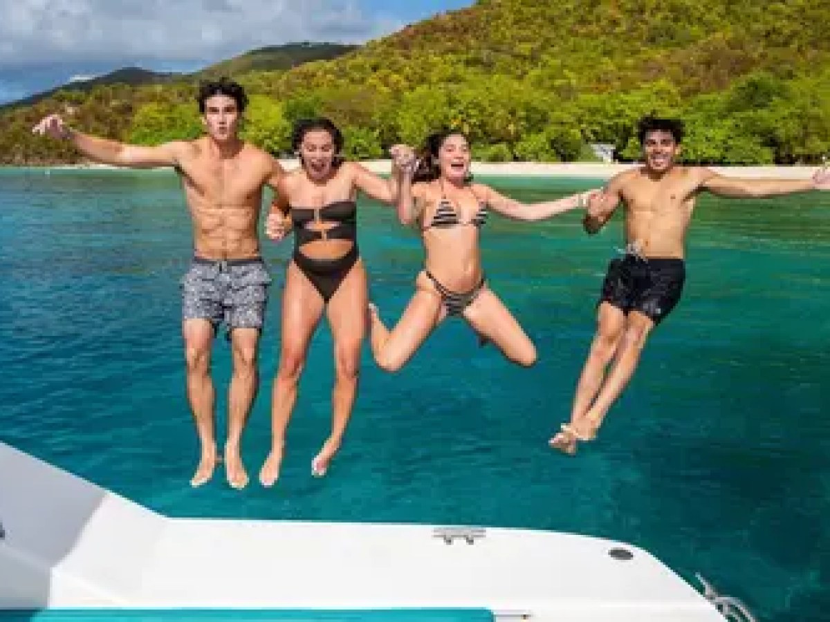 Four people jumping into clear blue water from a boat.