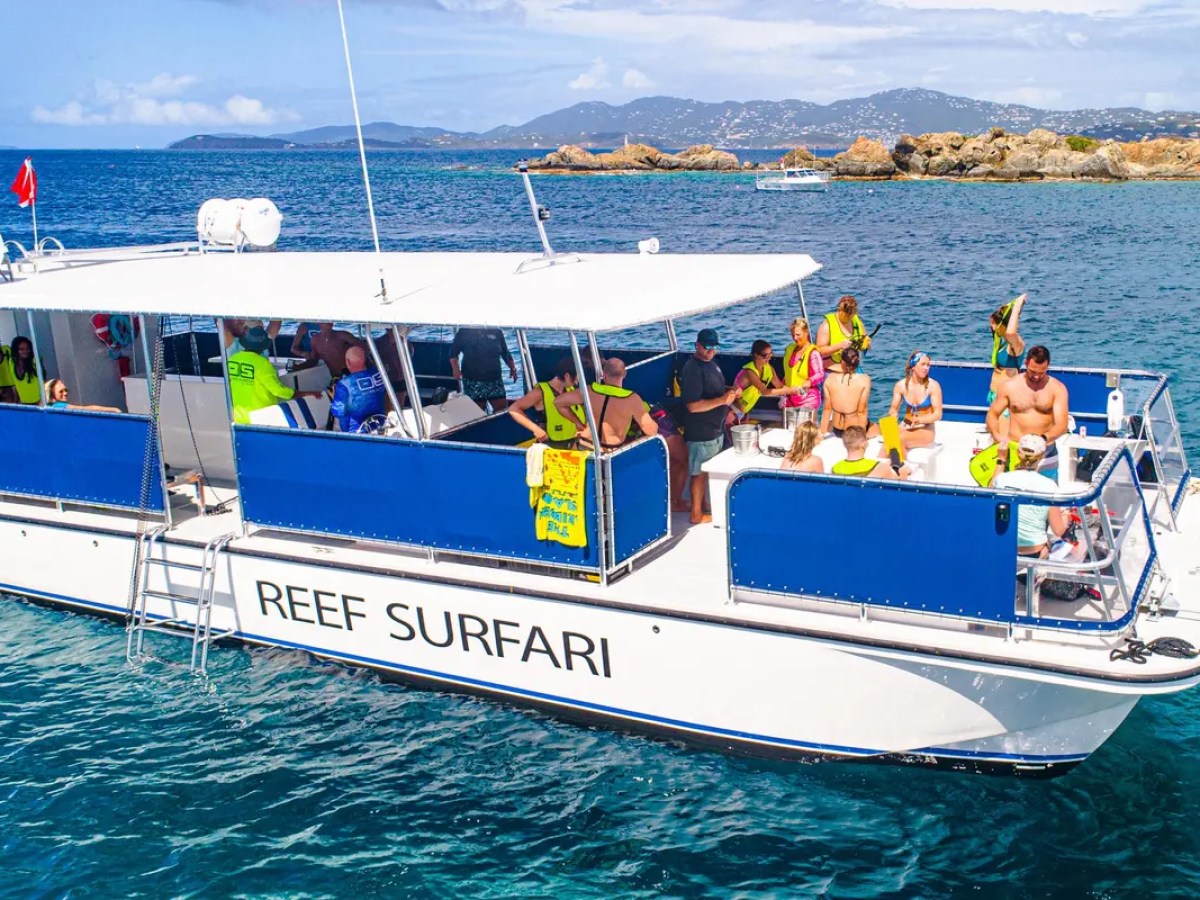 People on a boat named Reef Surfari in clear blue water near rocky islands.