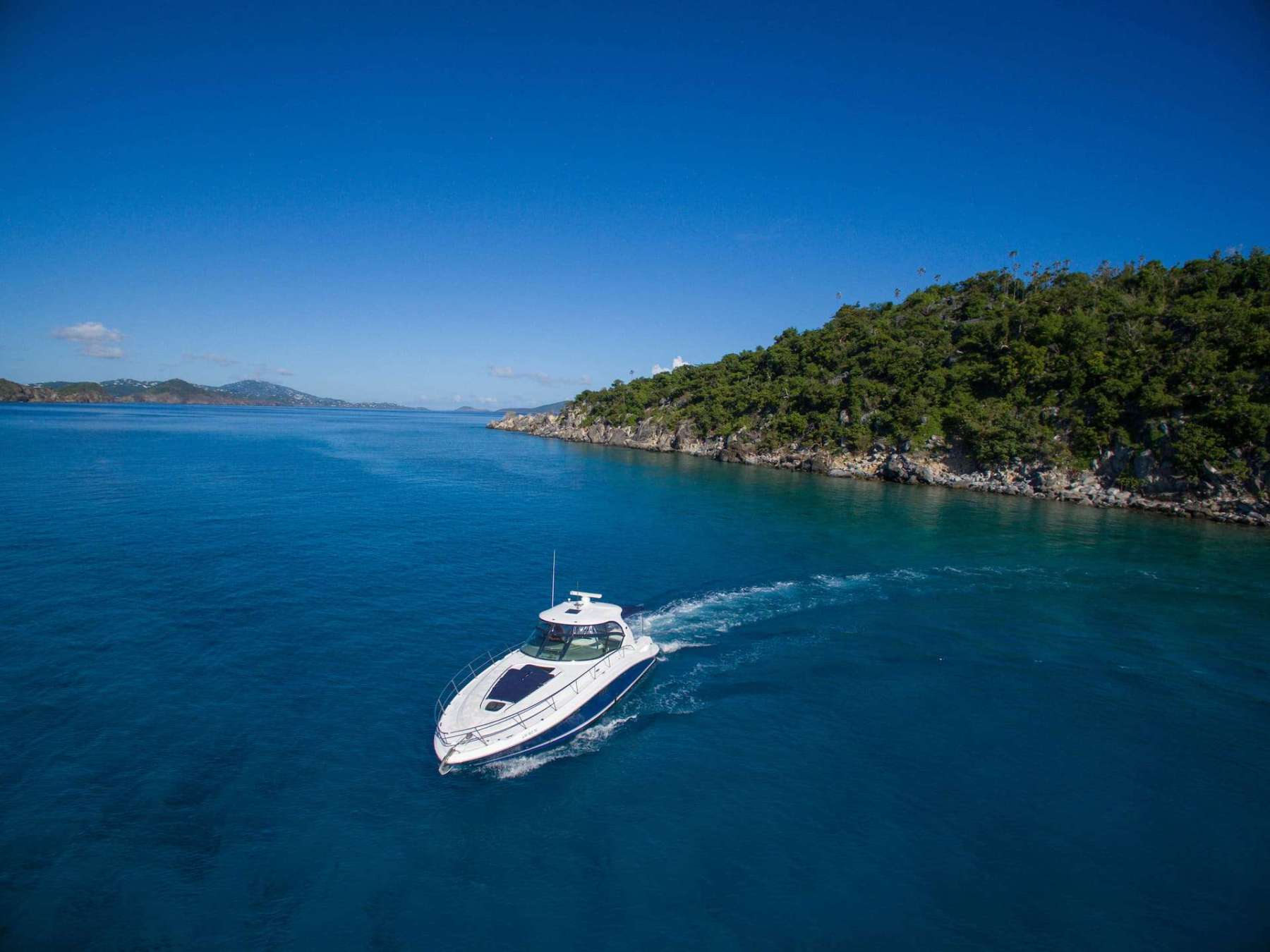 Boat sailing on clear blue waters near a lush, green island under a clear blue sky.