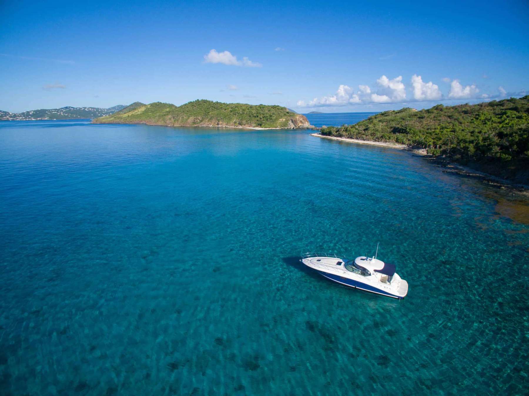 Aerial view of a boat on clear blue water near green islands under a blue sky.