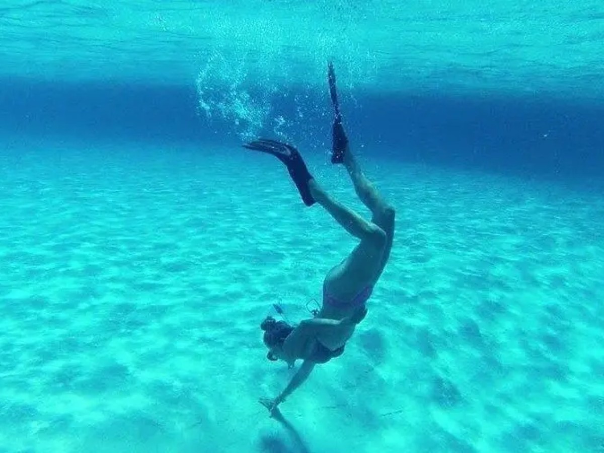 Person diving underwater with flippers in clear blue ocean.