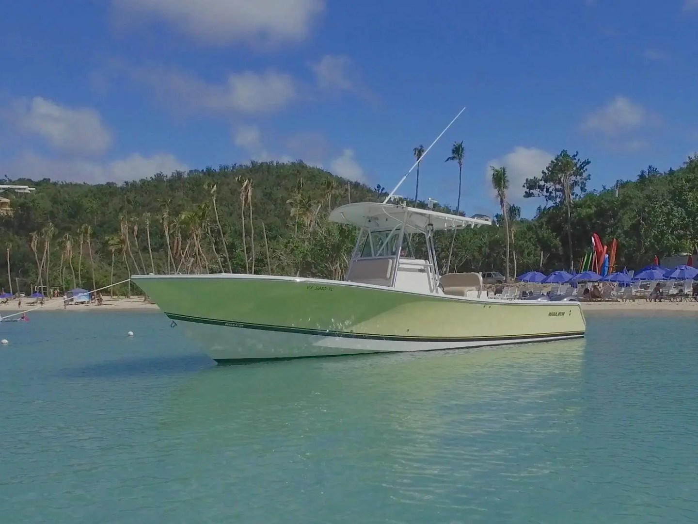 Green boat on calm water near a tropical beach with hills.